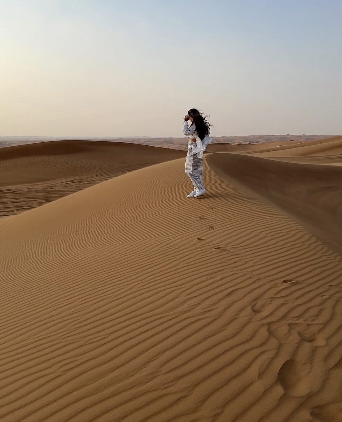 Desert safari packing essentials laid out on sand — sunscreen, sunglasses, trainers, water bottle and camera